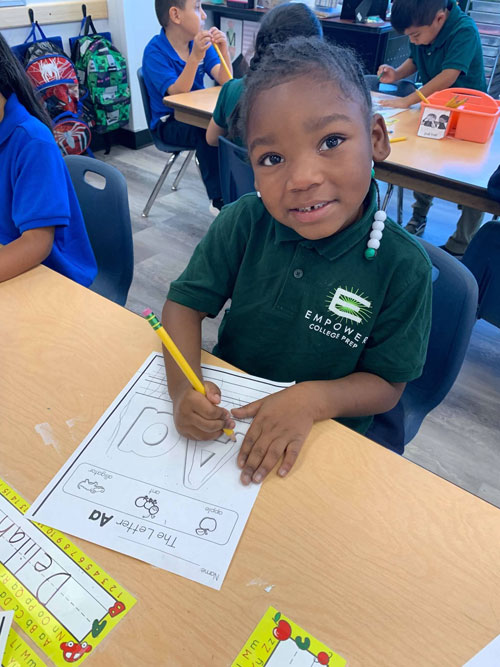 An Empower College Prep elementary-aged student working on a worksheet smiles for the camera.