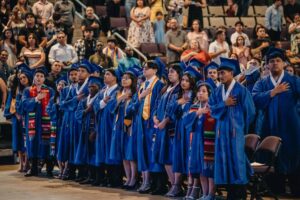 Empower College Prep seniors dressed in cap and gown, stand at their graduation ceremony.