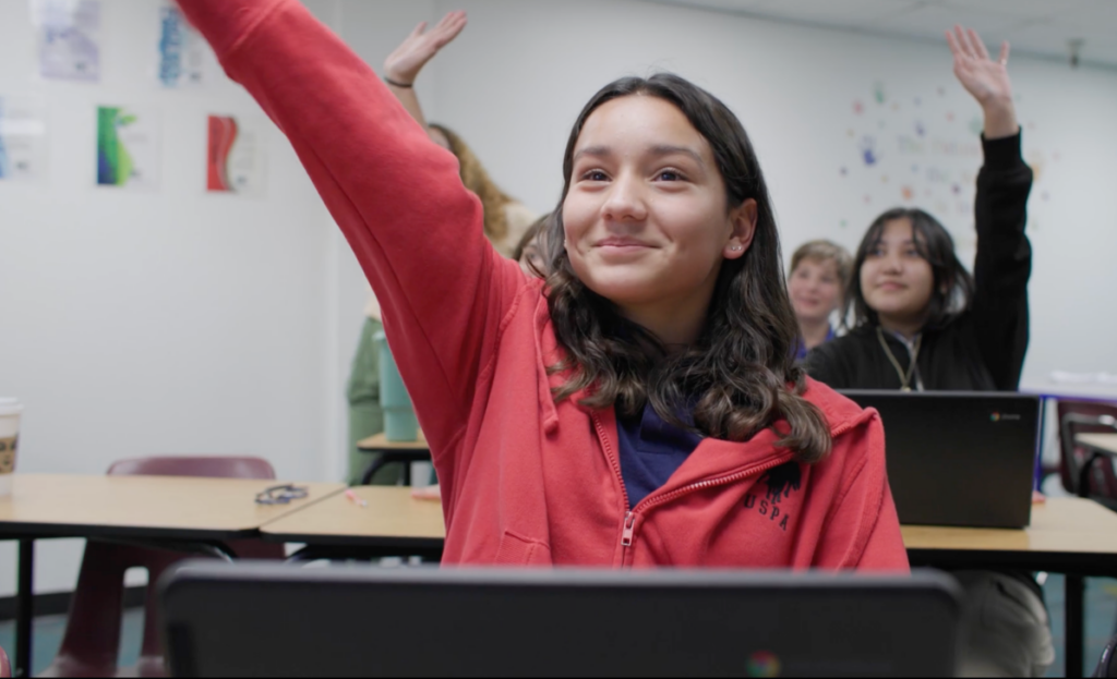 Female Empower College Prep student sits at her desk in the classroom, raising her hand.