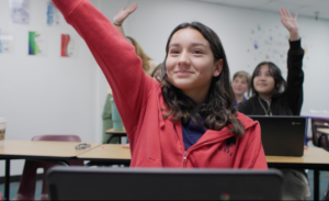 Female Empower College Prep student sits at her desk in the classroom, raising her hand.  