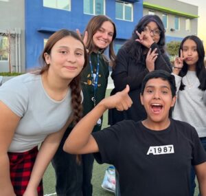 5 Empower College Prep middle school students smile and wave at the camera.