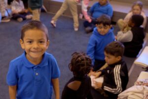 Empower College Prep Kindergarteners gather in a circle. One boy faces the camera and smiles.