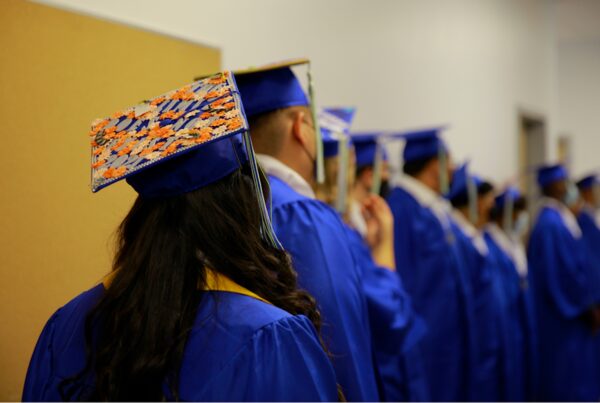 Empower College Prep students dressed in cap & gown viewed from behind as they stand in line in preparation for their graduation ceremony