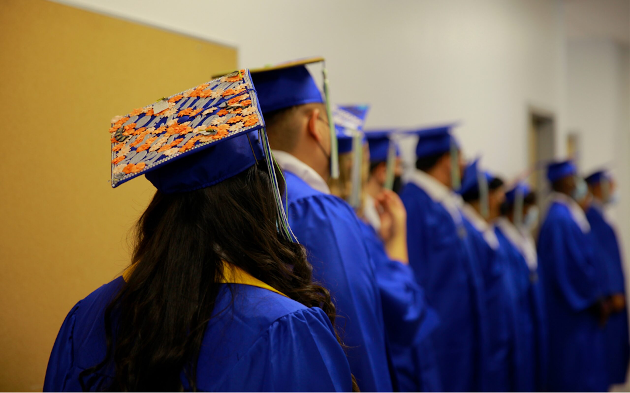 Empower College Prep students dressed in cap & gown viewed from behind as they stand in line in preparation for their graduation ceremony