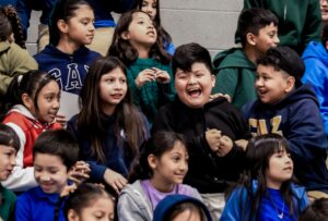 A group of Empower College Prep elementary school aged students celebrate together during a school assembly.