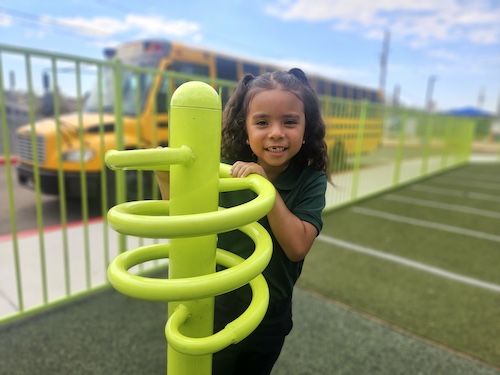 Empower College Prep student plays on an outdoor play structure. School bus in the background.
