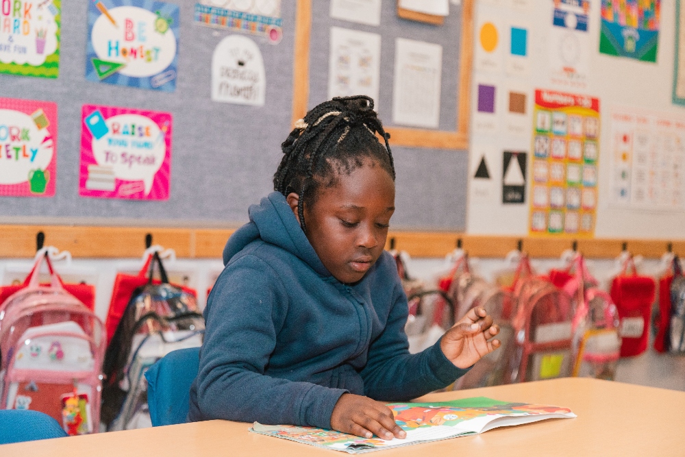 A female Empower College Prep elementary-aged student sits at her desk reading a book