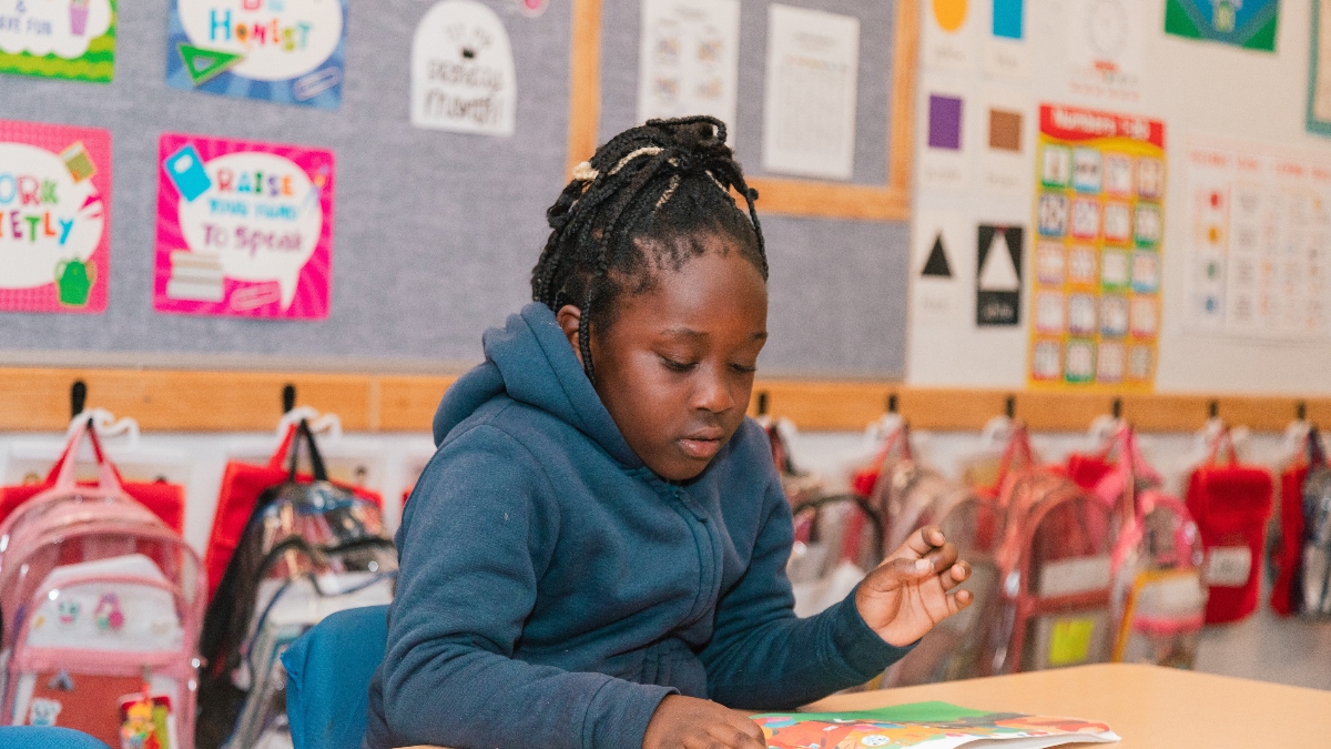 A female Empower College Prep elementary-aged student sits at her desk reading a book