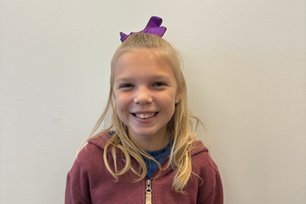 A photo of Rebekah smiling with a purple bow in her hair.