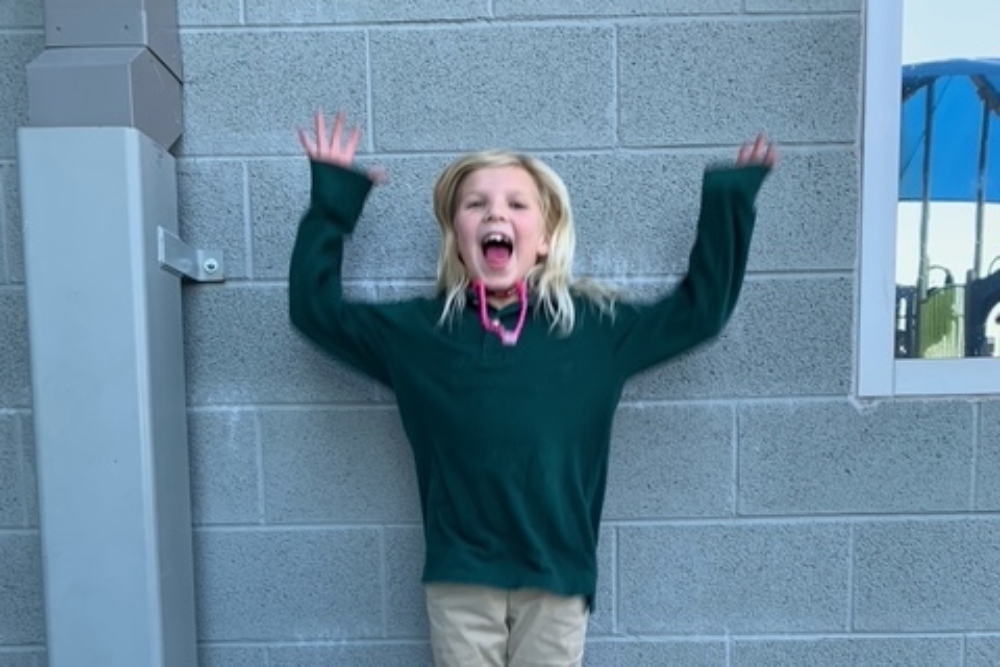 Rebecca is standing in front of a wall at Empower with her arms flung in the air and a huge smile.